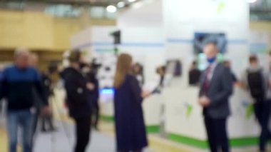 Film ekibi, büyük, parlak bir salonda bir işadamıyla röportaj yapıyor. Eğitim ve iş ile ilgili bulanık bir görüntü.