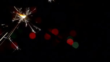 Yılbaşı ve Noel festivali geçmişi. Sparkler parlak bokeh çemberlerinin arka planında parlak bir şekilde yanar. Yakın plan. Sığ alan derinliği