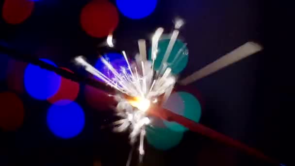 Nieuwjaar en Kerstmis feestelijke achtergrond. Sparkler brandt fel tegen een achtergrond van heldere bokeh cirkels. Een close-up. Ondiepe scherptediepte — Stockvideo