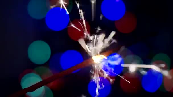 Świąteczne tło.New Years i Christmas.burning sparkler.Bengal świeca pali się jasno na tle jasnych kręgów bokeh. Close-up.Płytka głębokość pola — Wideo stockowe