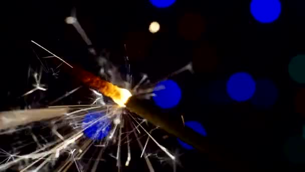 Año Nuevo y Navidad fondo festivo. Sparkler arde brillantemente sobre un fondo de círculos bokeh brillantes. Primer plano. Profundidad superficial del campo — Vídeo de stock