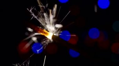 Yılbaşı ve Noel festivali geçmişi. Sparkler parlak bokeh çemberlerinin arka planında parlak bir şekilde yanar. Yakın plan. Sığ alan derinliği