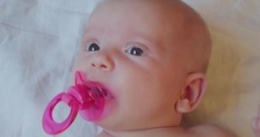 Ağzında bir emzik ile yatakta yatan küçük şirin bir bebeğin portresi.