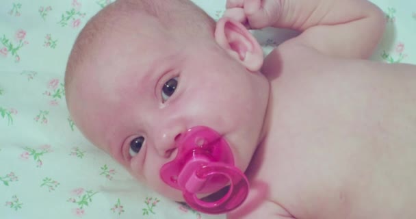 Egy kis aranyos baba fekszik az ágyban egy rózsaszín cumival a szájában. — Stock videók