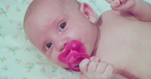 Cute little newborn baby. portrait of a toddler with a pacifier in his mouth, who looks in surprise at the camera — Stock Video