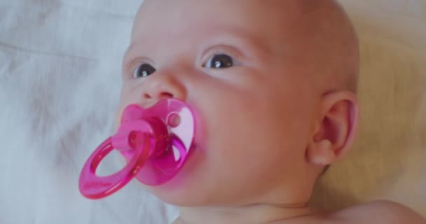 Söt liten nyfödd bebis. Porträtt av ett barn med en napphållare i munnen som ser sig omkring med en förvånad blick — Stockvideo