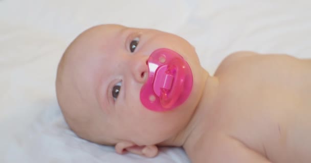 Porträtt av ett modernt barn.söt baby med en napphållare i munnen ligger i sängen.view från ovan — Stockvideo