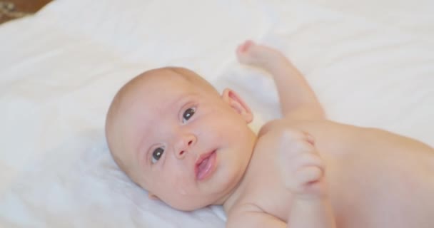 Portrait of a cute baby lying on a sheet looking up in surprise — Stock Video