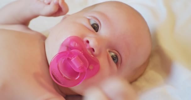 Portrait of a cute baby with a pacifier in his mouth.A small child with a surprised look lies on the sheet.extreme close-up — Stock Video