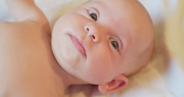Portret van een schattige baby die op een laken ligt met een verrassende blik — Stockvideo