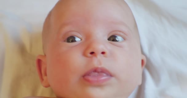 Söt rolig baby med förvånad utseende ligger i sängen. Porträtt. närbild — Stockvideo