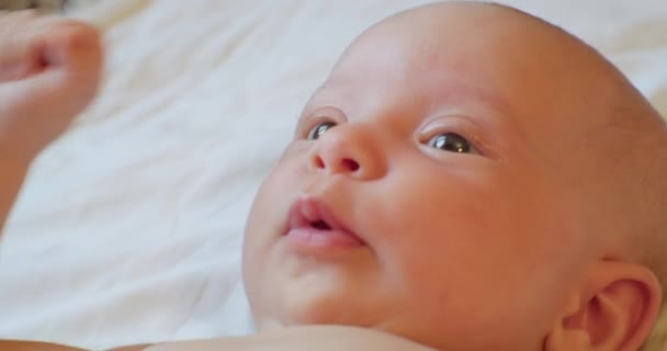 Porträt eines süßen Babys, das überrascht auf einem Laken liegt — Stockvideo