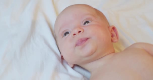 Porträt eines süßen Babys, das überrascht auf einem Laken liegt — Stockvideo