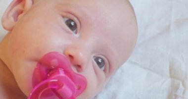 Modern bir çocuğun portresi. Ağzında pembe bir emzik olan tatlı bir bebek yatakta yatıyor. yakın plan