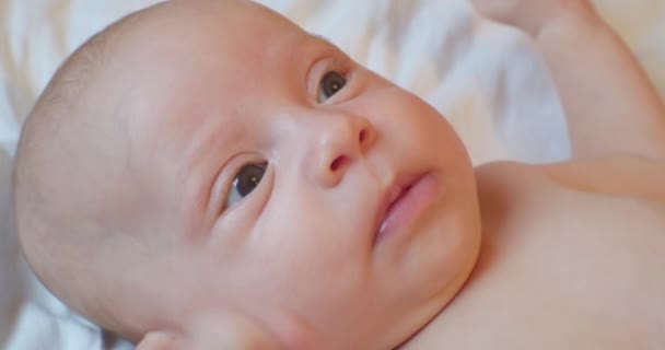 Portret van een schattige baby die op een laken ligt met een verrassende blik — Stockvideo