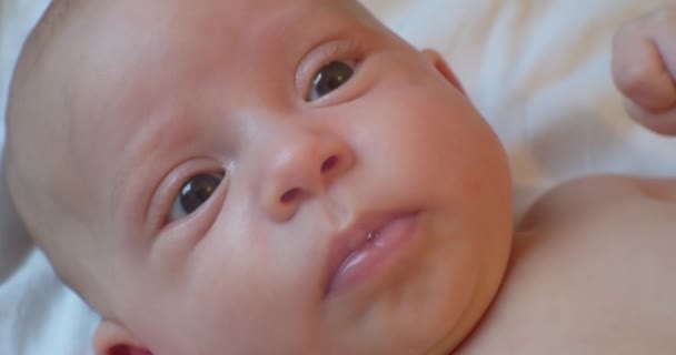 Schattig grappig baby met verrast blik ligt in bed. portret. close-up — Stockvideo