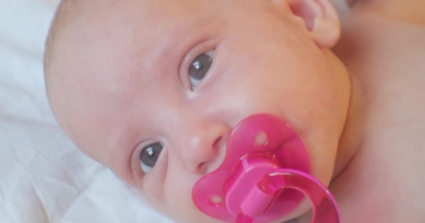 Ritratto di un bambino moderno. bambino carino bambino con un ciuccio rosa in bocca si trova a letto. primo piano — Video Stock