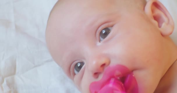 Porträtt av ett modernt barn. Söt baby spädbarn med en napphållare i munnen ligger i sängen. närbild — Stockvideo
