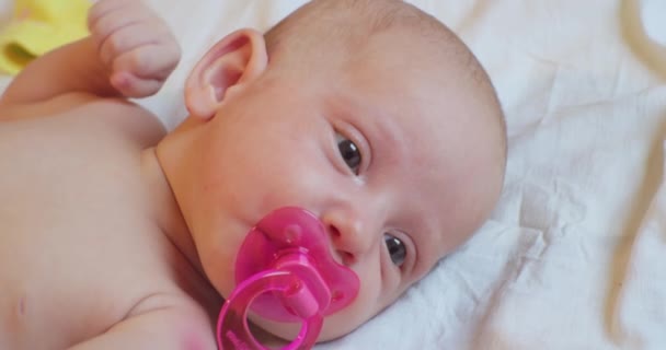 Portrait of a modern child. cute baby infant with a pink pacifier in his mouth lies in bed. close-up — Stock Video