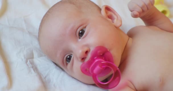 Cute baby infant with pink pacifier in mouth lies in bed. portrait. close-up — Stock Video