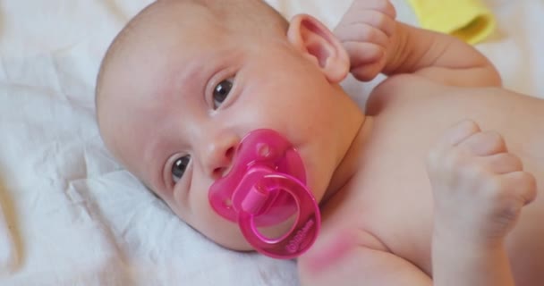 Portrait of a modern child. cute baby infant with a pacifier in his mouth lies in bed. close-up — Stock Video