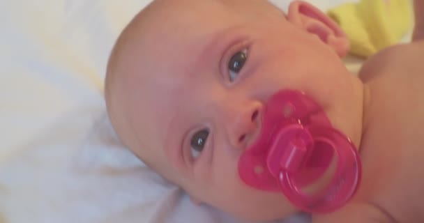 Retrato de uma criança moderna. bebê bonito bebê com uma chupeta rosa em sua boca está na cama. close-up — Vídeo de Stock