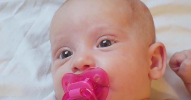 Portrait of a modern child. cute baby infant with a pacifier in his mouth lies in bed. close-up — Stock Video