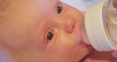 Şaşkın bakışlı şirin bir bebek emzik şişesinden su içiyor. yakın plan