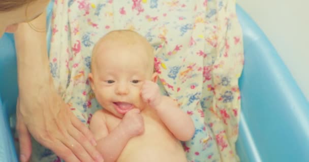 Opiekuńcze matki myją swoje małe słodkie dziecko leżące na jasnym prześcieradle w dziecięcej kąpieli — Wideo stockowe