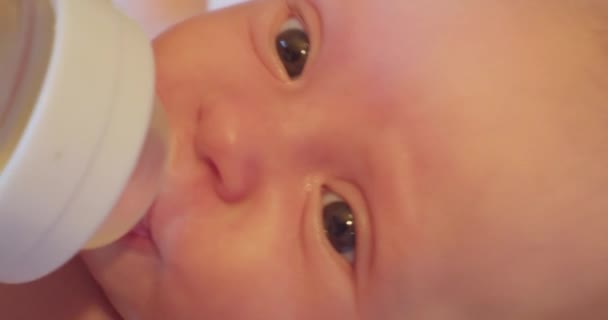 Een kleine schattige baby met een verrassende blik drinkt water door een tepel uit een plastic fles — Stockvideo