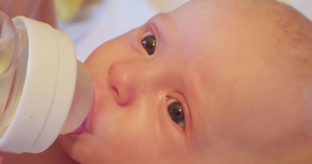 Un pequeño bebé lindo con una mirada sorprendida bebe agua a través de un chupete de un biberón. primer plano — Vídeo de stock