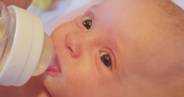 Een kleine schattige baby met een verrassende look drinkt water door een fopspeen uit een babyflesje. close-up — Stockvideo