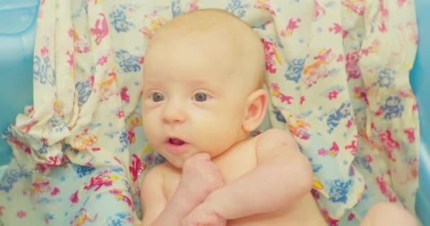 Portret van een schattig grappig kind dat zit in een babybadje op een helder laken. — Stockvideo