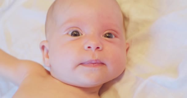 Het gezicht van een klein schattig grappig kind dat in zijn bed ligt en verrast opkijkt. close-up — Stockvideo