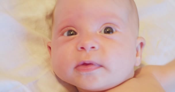 Het gezicht van een klein schattig grappig kind dat in zijn bed ligt en verrast opkijkt. close-up — Stockvideo