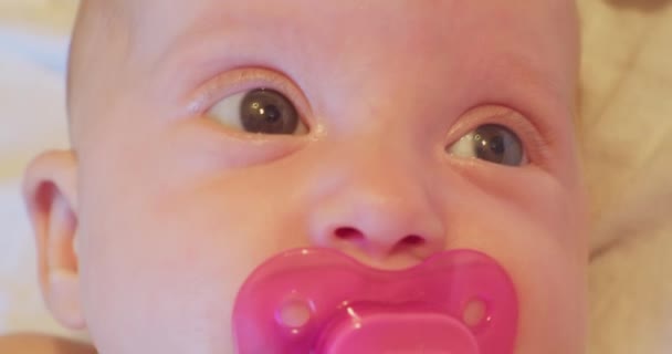 Gezicht van een kleine grappige en schattige baby met een fopspeen in zijn mond en een verrassende blik. close-up portret — Stockvideo