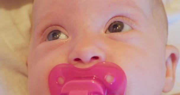 Het gezicht van een kleine grappige en schattige baby met een fopspeen die verrast opkijkt. close-up portret — Stockvideo