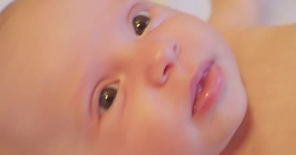 Portret małego, słodkiego, zabawnego dziecka, które leży w łóżku i patrzy w górę z zaskoczeniem. zbliżenie — Wideo stockowe
