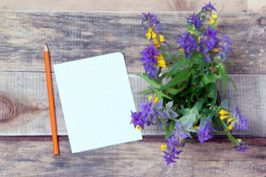 Kır çiçekleri ve bir kağıt bir kalem bir ahşap yüzeyi ile.