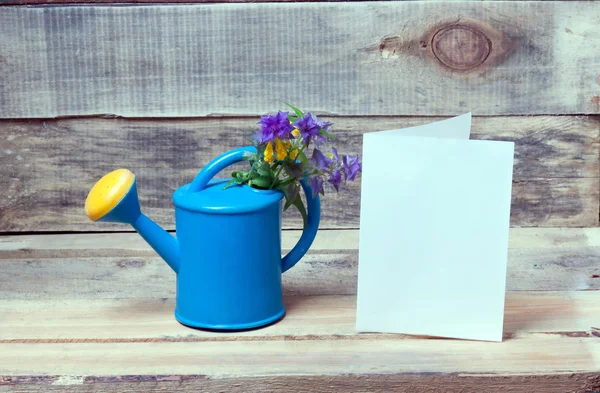 watering can, flowers and a blank sheet of paper on a wooden bench