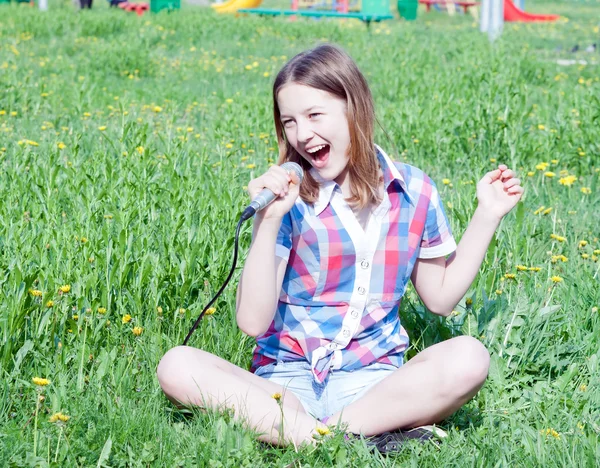 Ragazza teenager che canta in un microfono che si siede sull'erba Foto Stock Royalty Free