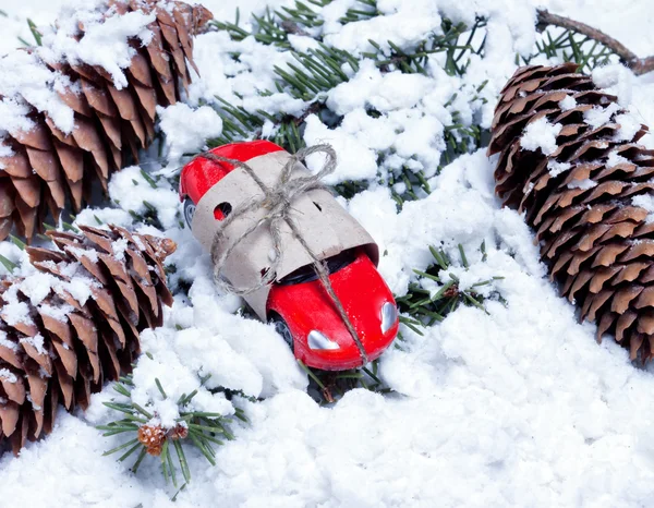 Carro de brinquedo pequeno, embalado como um dom e cones em ramos de abeto — Fotografia de Stock