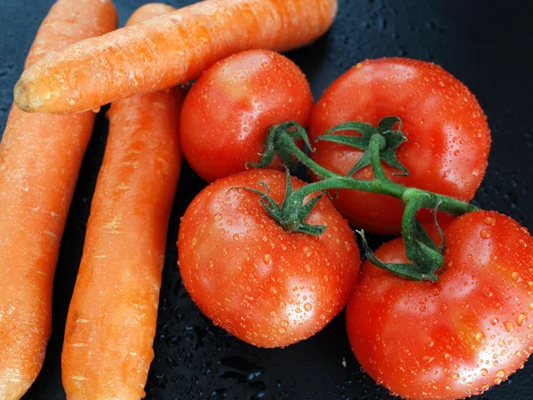 Tomatoes and carrots on a black background — Stock Photo, Image