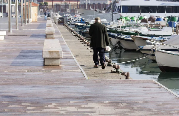 An older man walks along attached boats in port — Stock Photo, Image