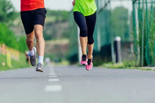 Close up feet with running shoes and strong athletic male and female legs jogging on the running track