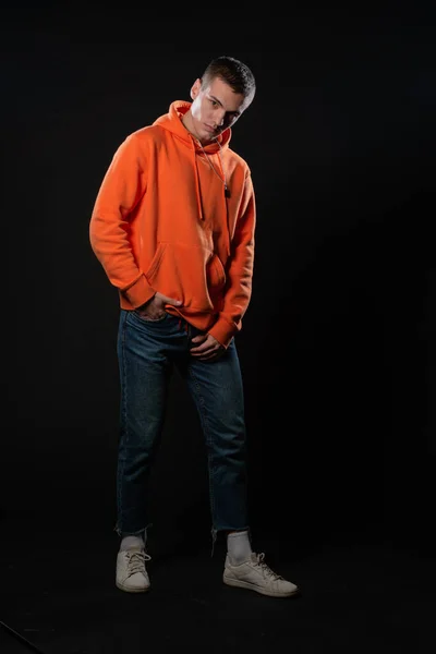 Junger Schöner Mann Jeans Und Orangefarbenem Kapuzenpulli Posiert Vor Schwarzem — Stockfoto