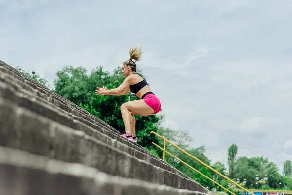 健康的运动员 穿着紧身运动服的漂亮女人在楼梯上跳跃 在慢跑前热身 同时看起来很有动力 — 图库照片