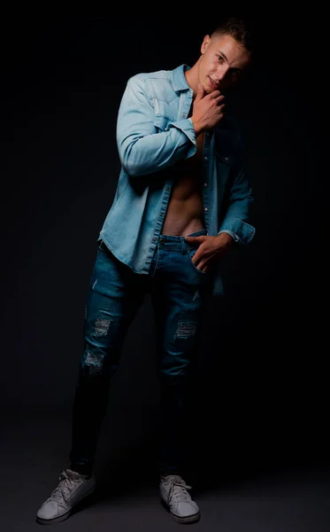 Attractive man posing in blue jeans and fancy unbuttoned jeans shirt