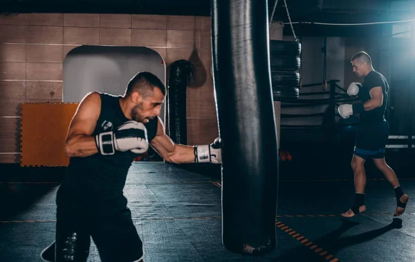 Male boxer training with punching bag in dark sports hall. Male boxer as exercise for the big fight. Boxer hits punching bag