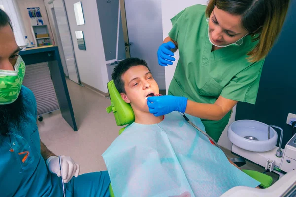 女性歯科医は十代の男の子の患者の口と歯を調べる — ストック写真